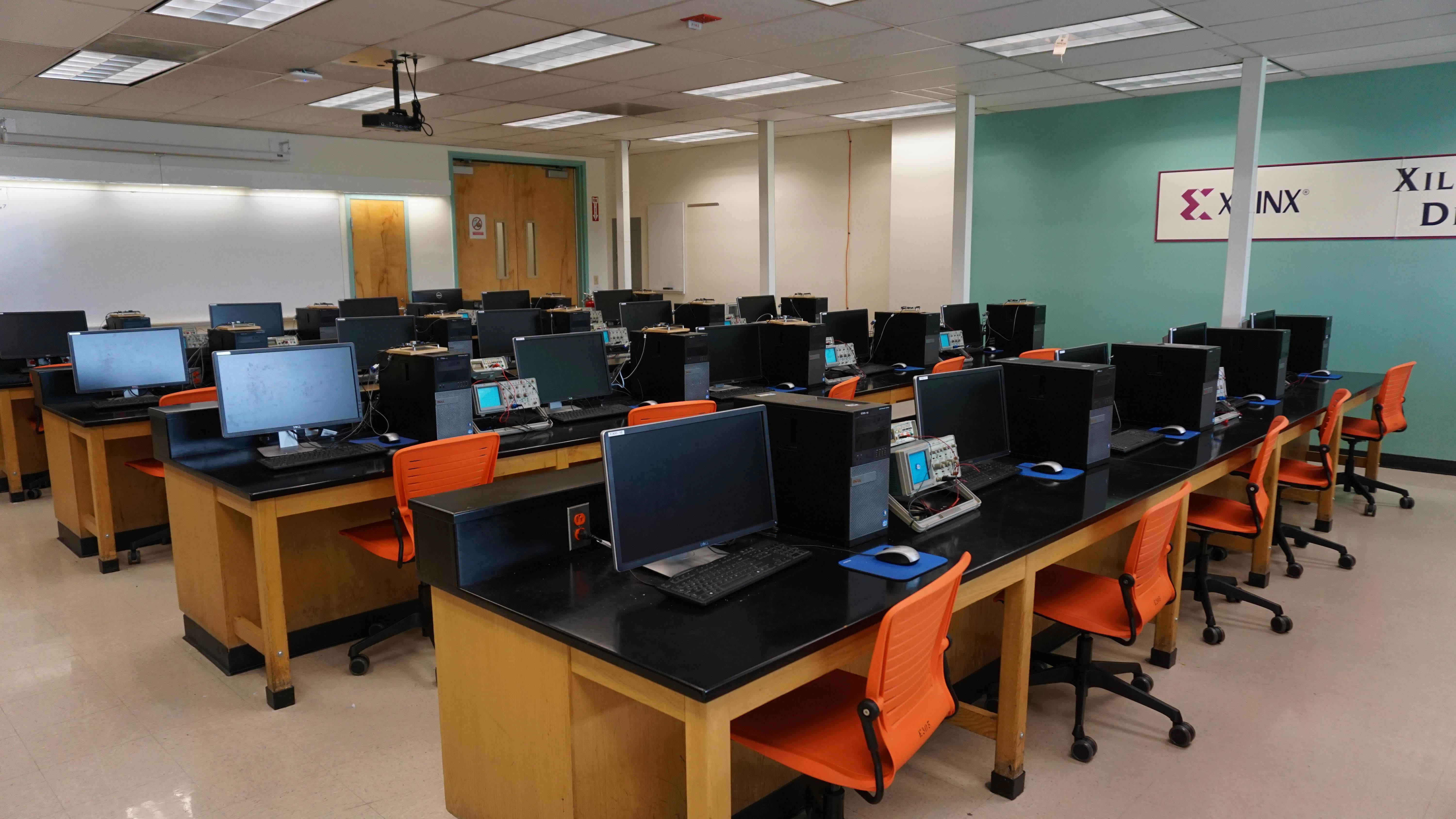 A classroom with computers, orange chairs, and a bright teal wall with the Xilinx logo.