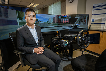 professor sits in front of driving simulation setup